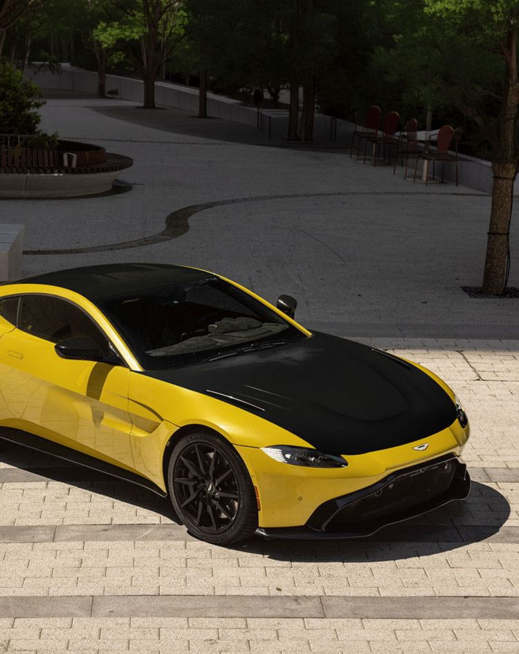Yellow sports car with a contrasting black hood parked on a paved street, highlighting its sleek exterior and the enhanced finish achievable with LLumar Select Black paint protection film. 