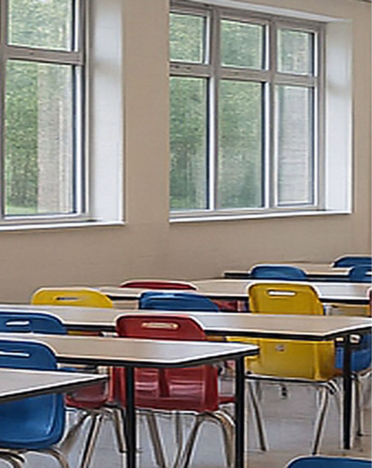 Bright cafeteria with long tables and colorful chairs next to large windows overlooking trees. 