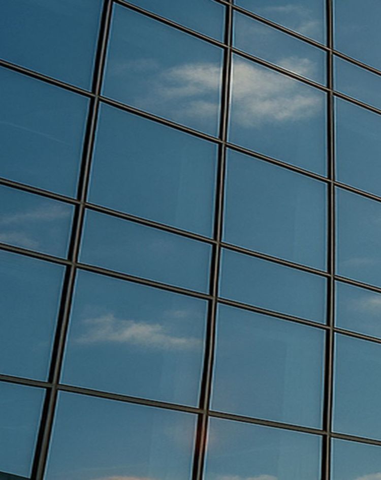 A modern glass office building reflecting the blue sky and bright sun, showcasing large architectural window panels. 