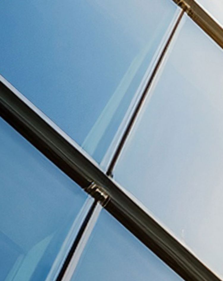 A low-angle view of a modern glass building reflecting the sky and sunlight. 