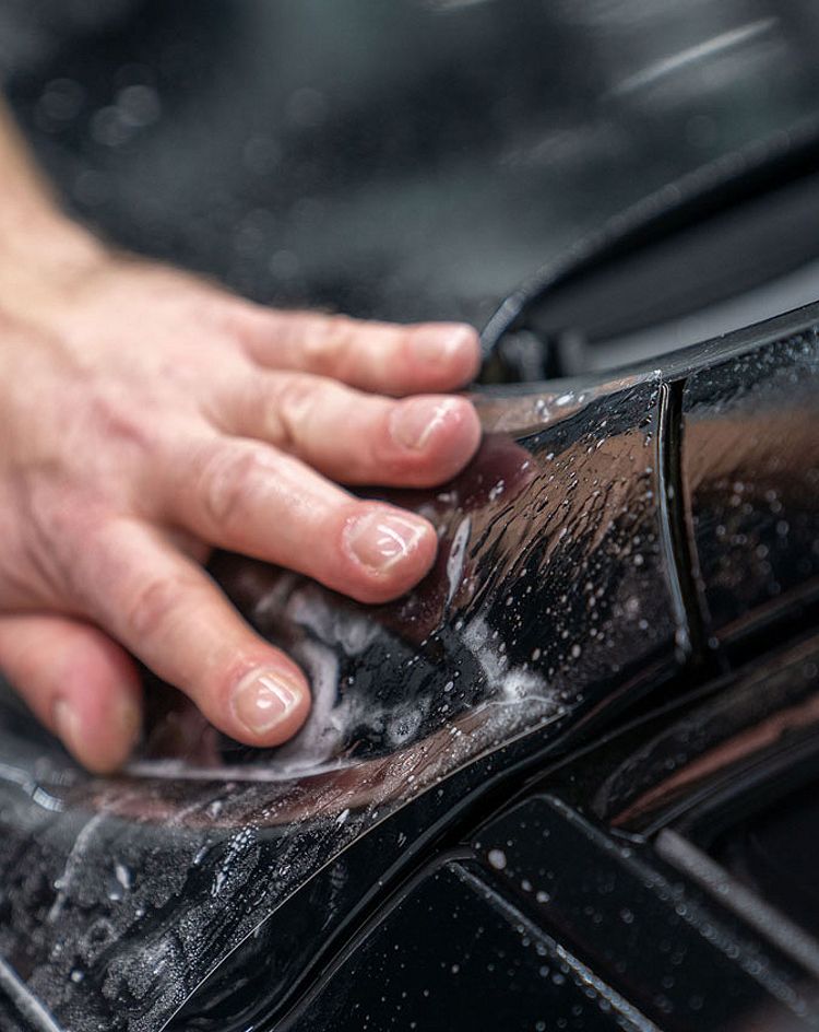 Individual installing PPF on the hood of a black vehicle 