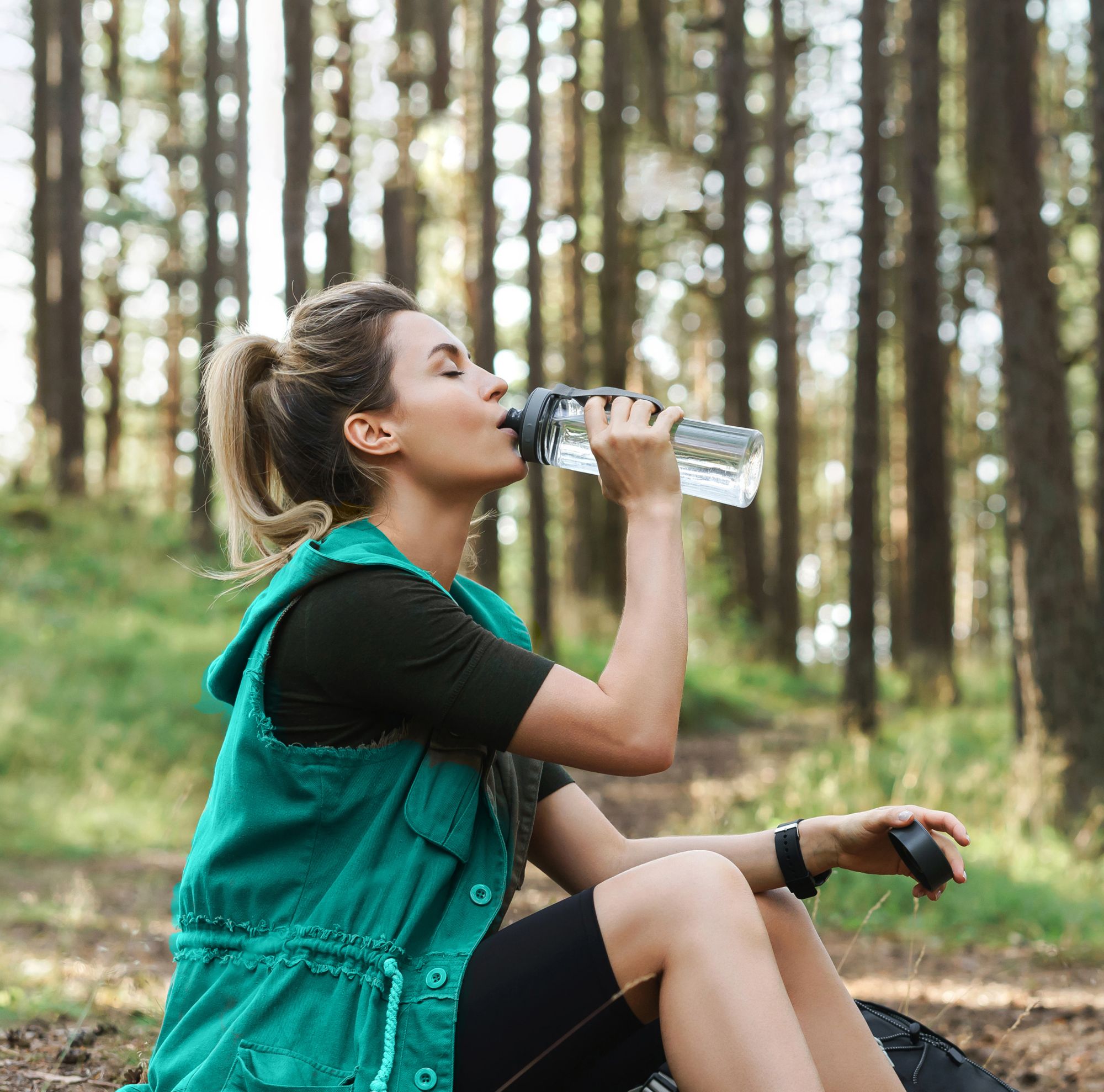 Woman sitting down and drinking water from a recycled bottle. 