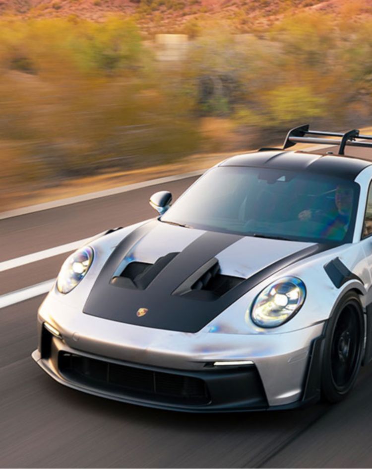 Silver and black sports car driving at high speed on a desert highway with red rock formations in the background. 