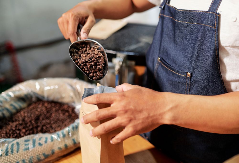 A person scoops coffee beans into a paper bag. 