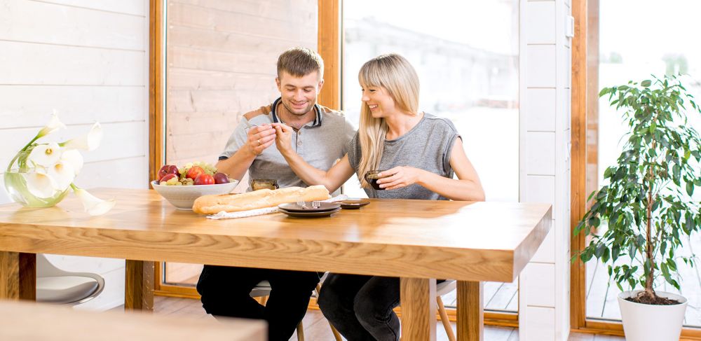 Two people eat while seated at a wood table. 