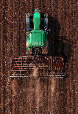 An aerial view of a green tractor tilling soil in a large field.