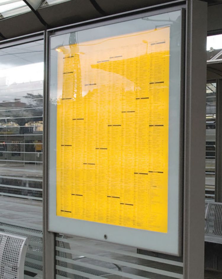 Train station platform with large glass schedule boards and seating. 