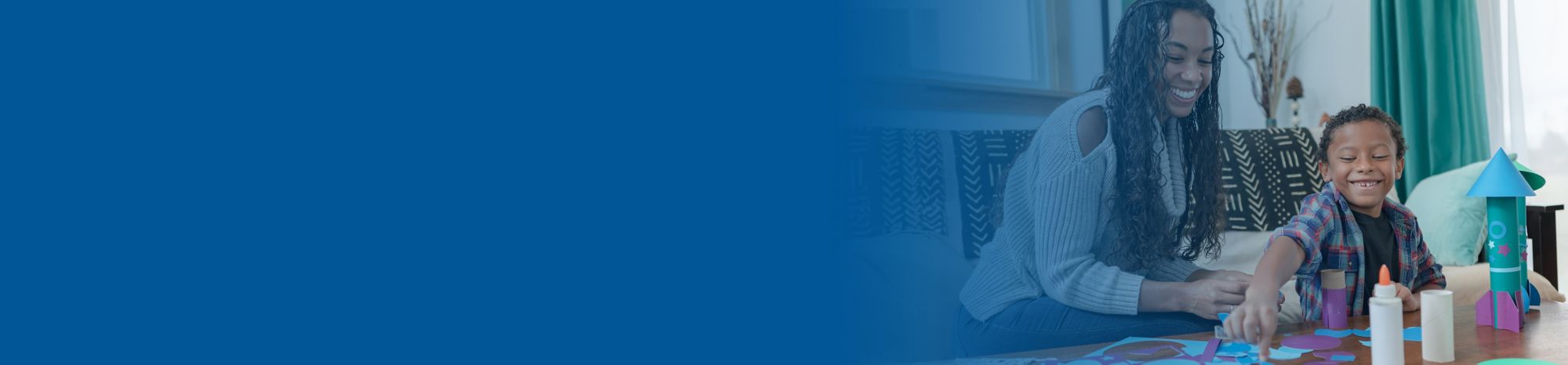 Blue banner fade over a picture of a smiling mom and her son building a craft space rocket with glue and paper. 