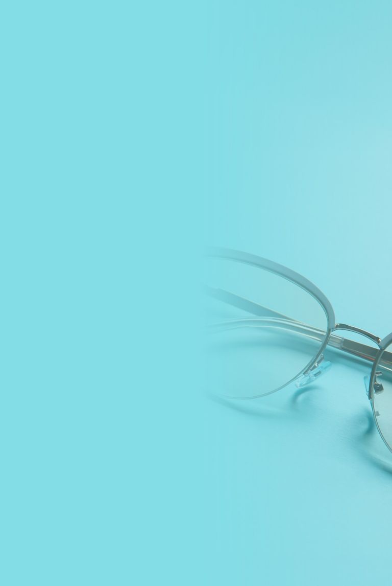 Gray semi-rimless eyeglasses resting on a light blue surface. 