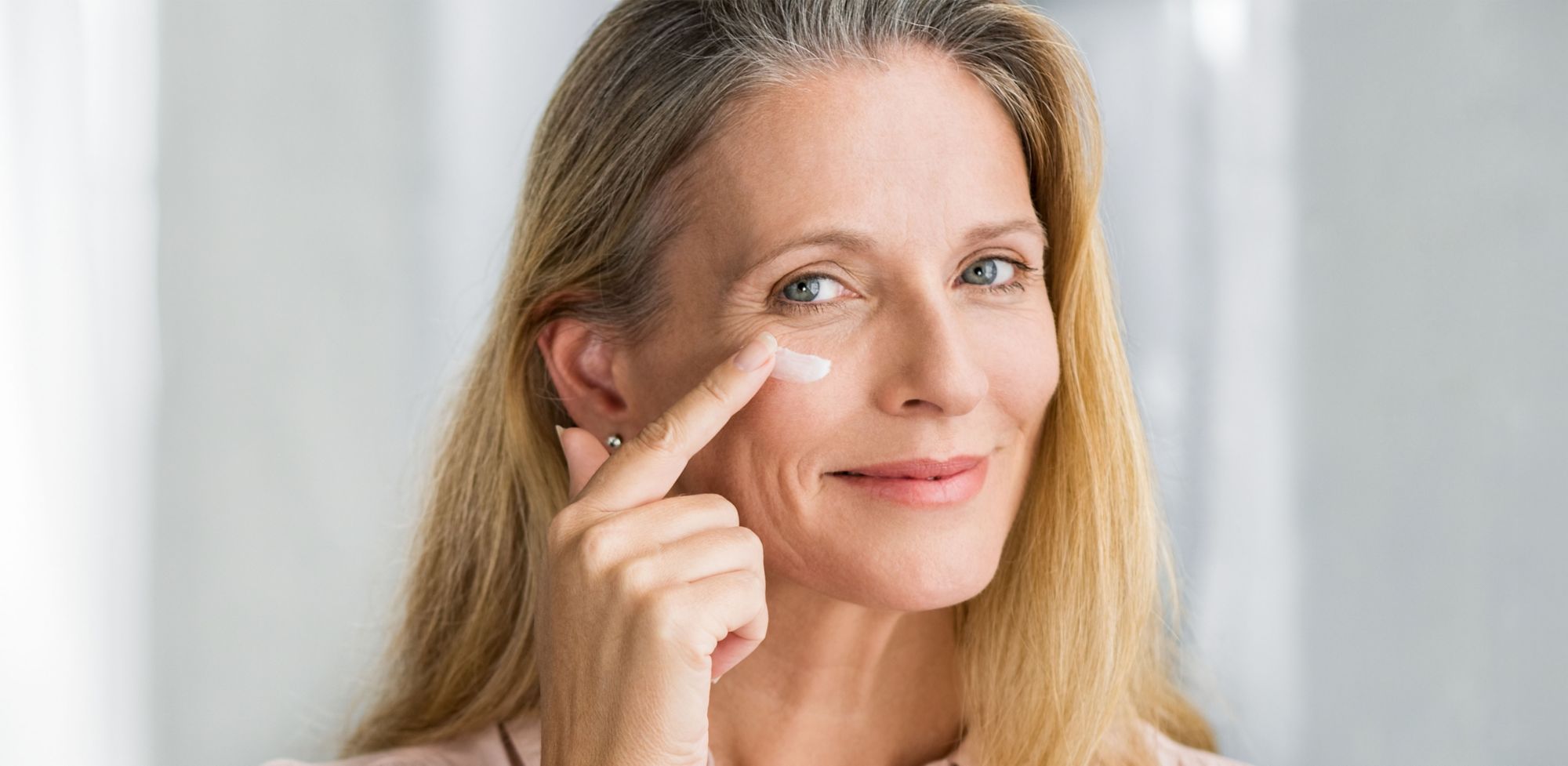 A woman person applies cream under her their eye. 