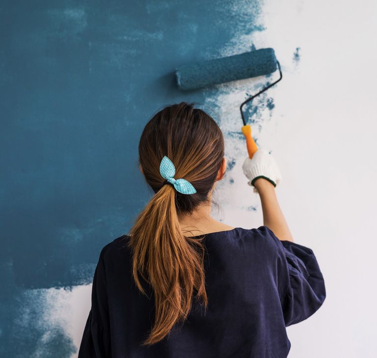A person paints a wall with a roller brush. 