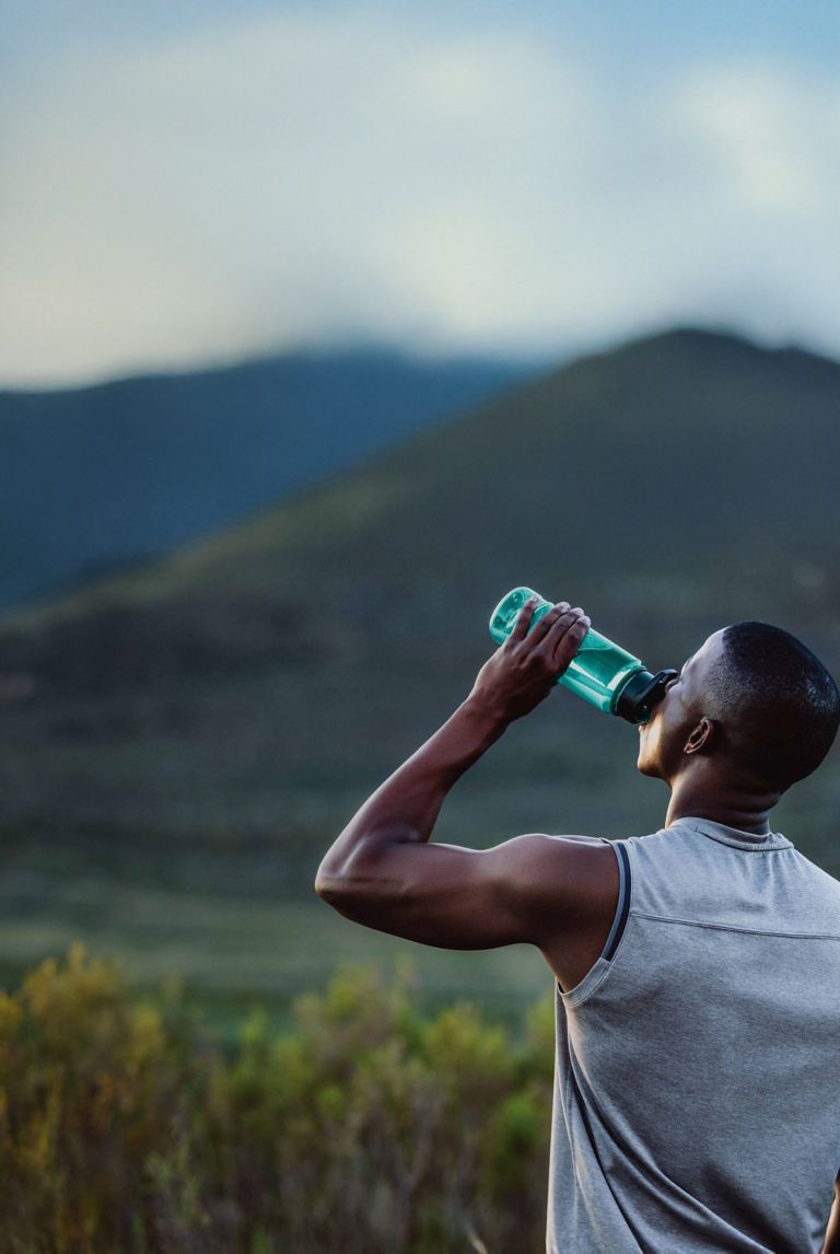 A man drinks from a water bottle in a field.  