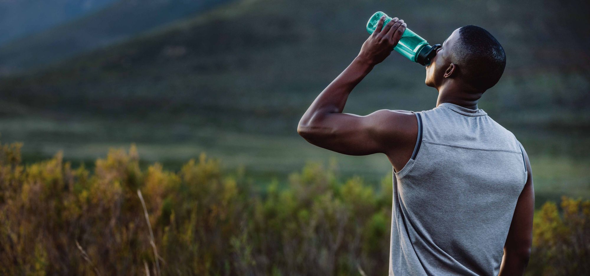 A man drinks from a water bottle in a field.  