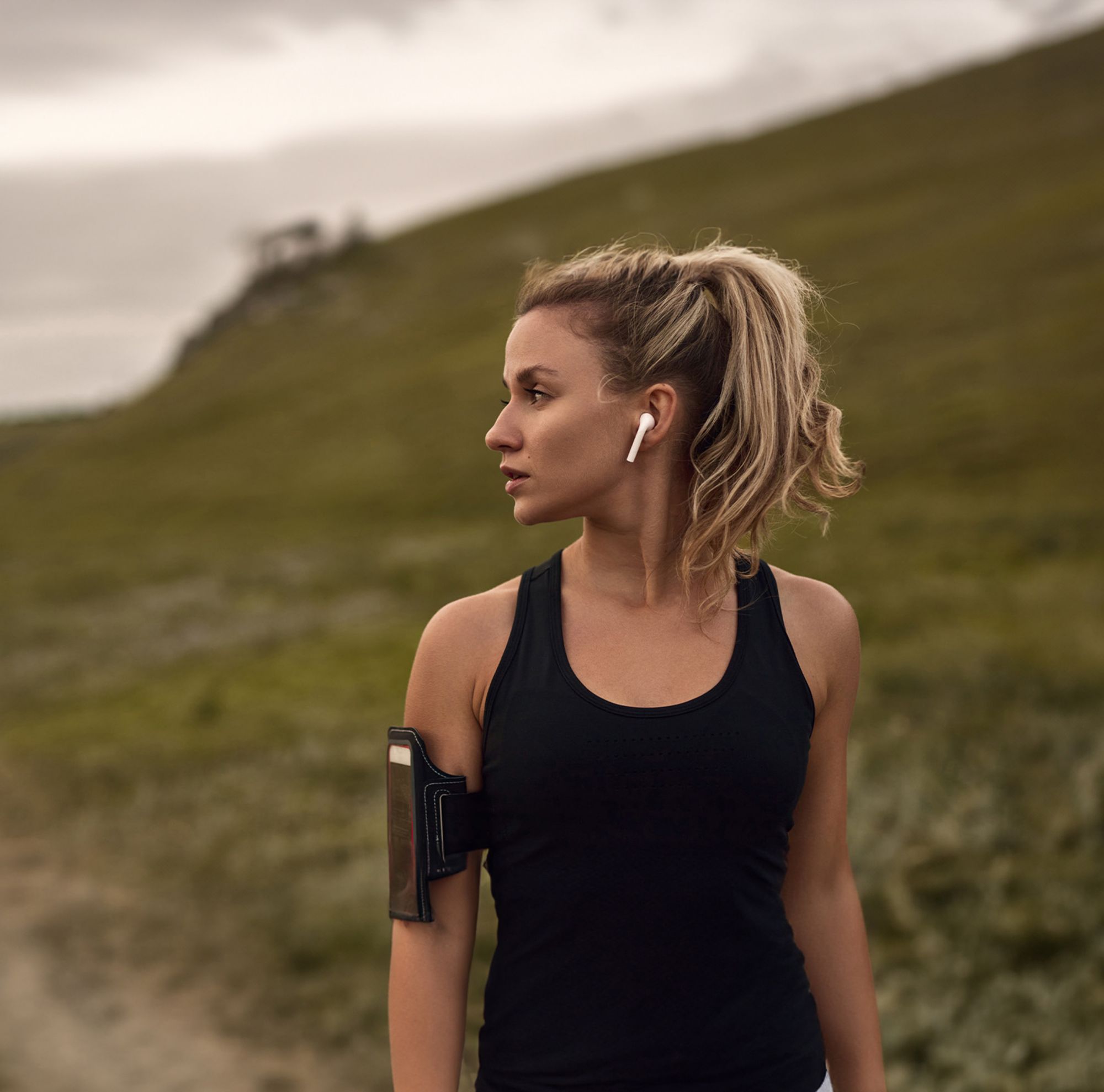 A woman exercising in the mountains wears wireless earbuds. 