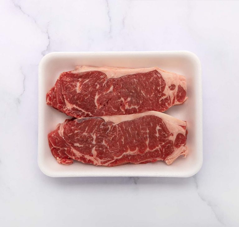 Two raw beef steaks on a white Aventa food tray. 