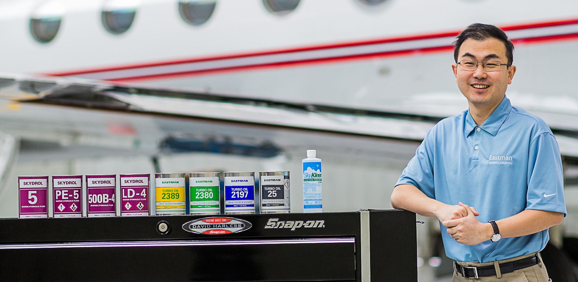 A man stands next to several cans of Skydrol that rest on a surface. 
