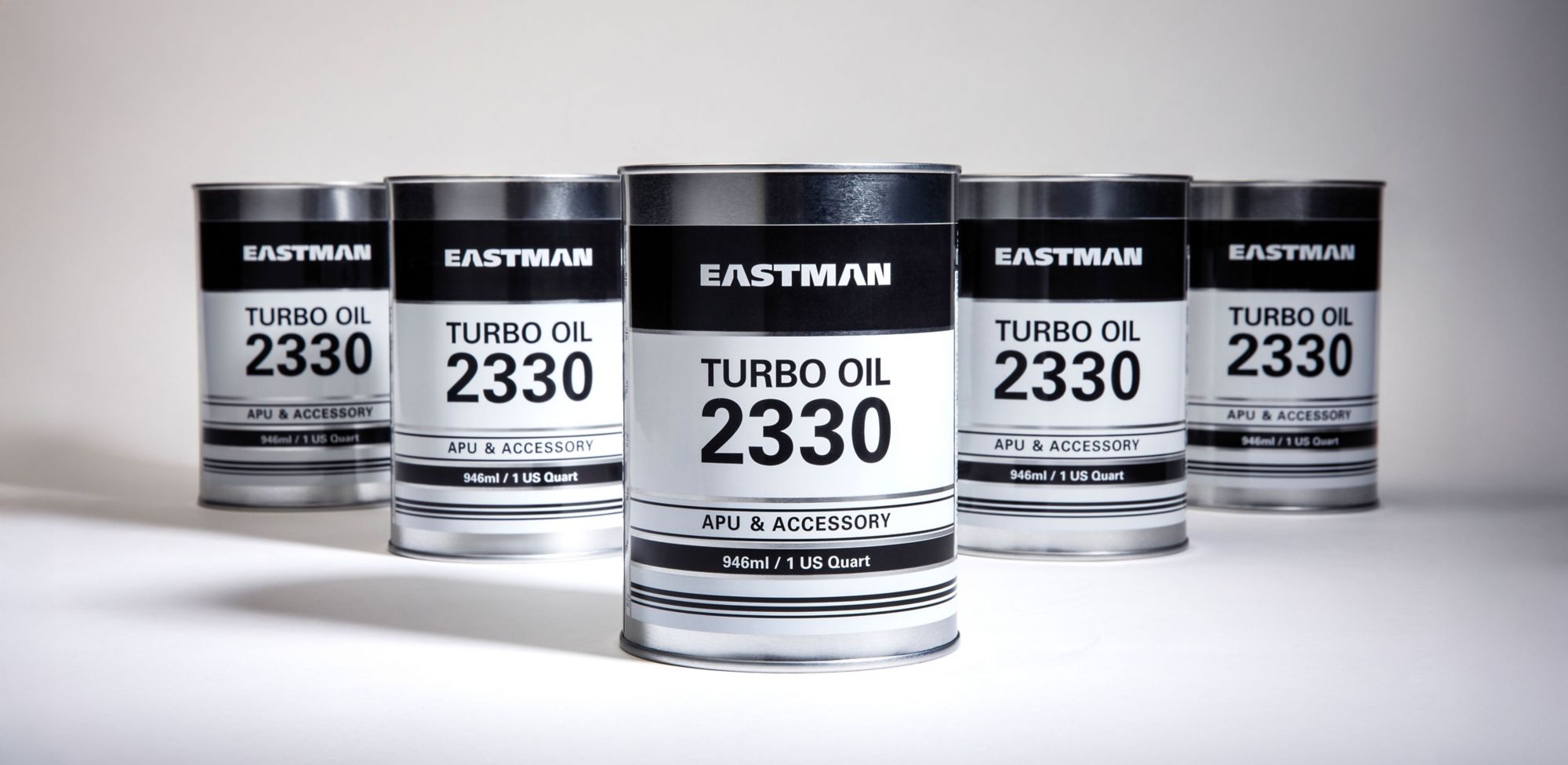 Five cans of Eastman Turbo Oil 2330 over a white surface. 