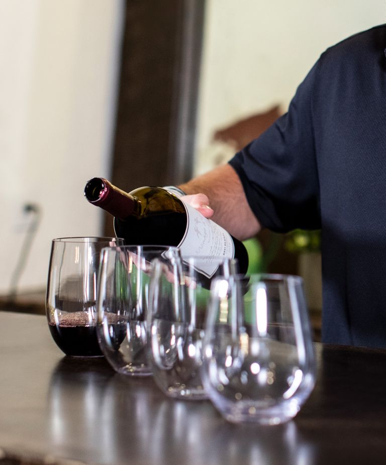 A bartender pouring wine into one of four clear cups. 