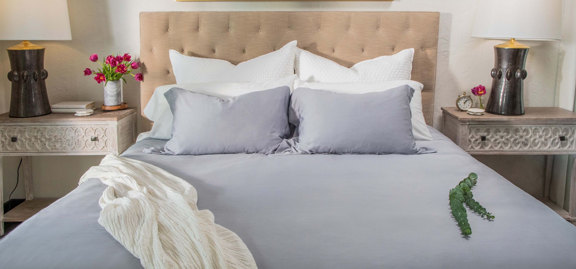 A bed made with gray and white linens and a white blanket. 