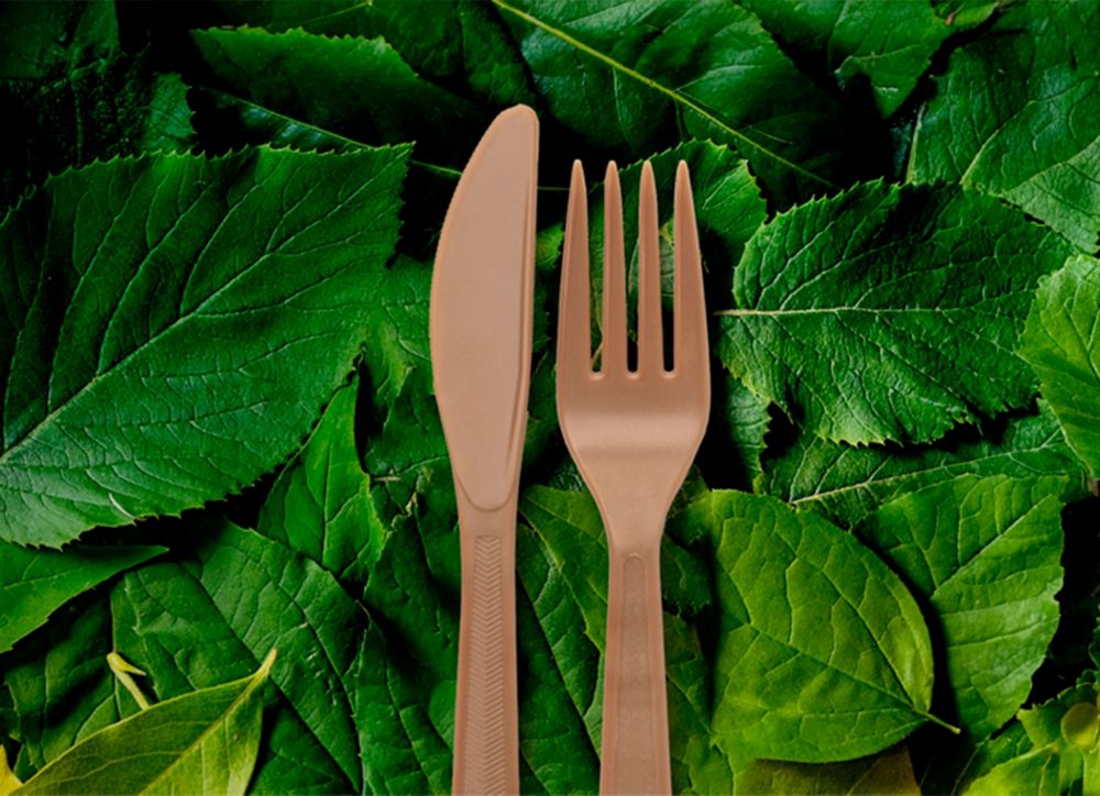 A plastic fork and knife lay on a field of green leaves 