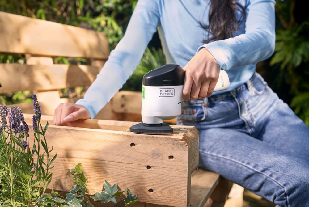 A person uses a Black+Decker sanding tool on a wooden bench. 