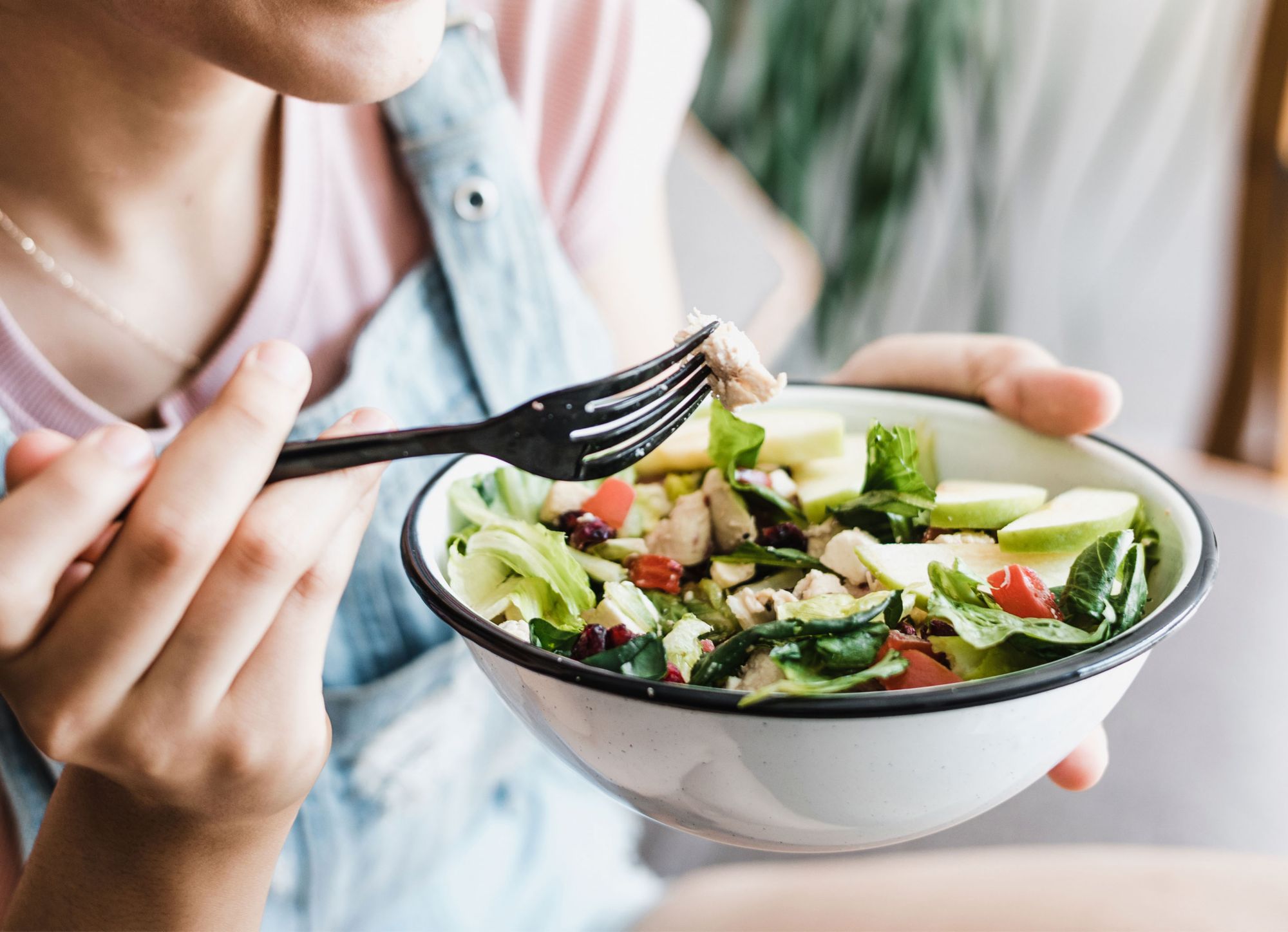 A person holds a bowl of salad in one hand and a plastic fork in the other  