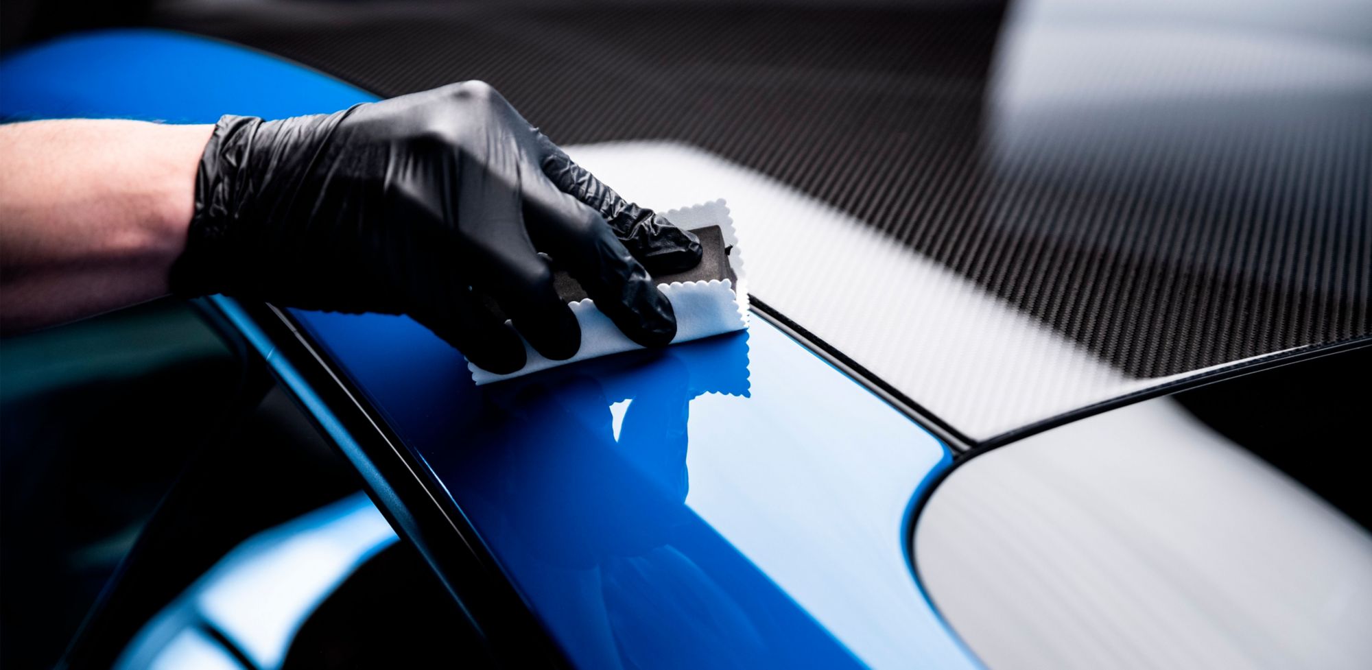 A technician carefully wipes the frame of a blue car. 