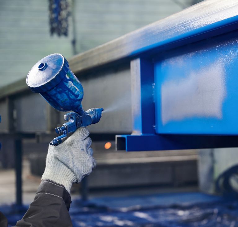 Blue paint is sprayed on industrial metal. 