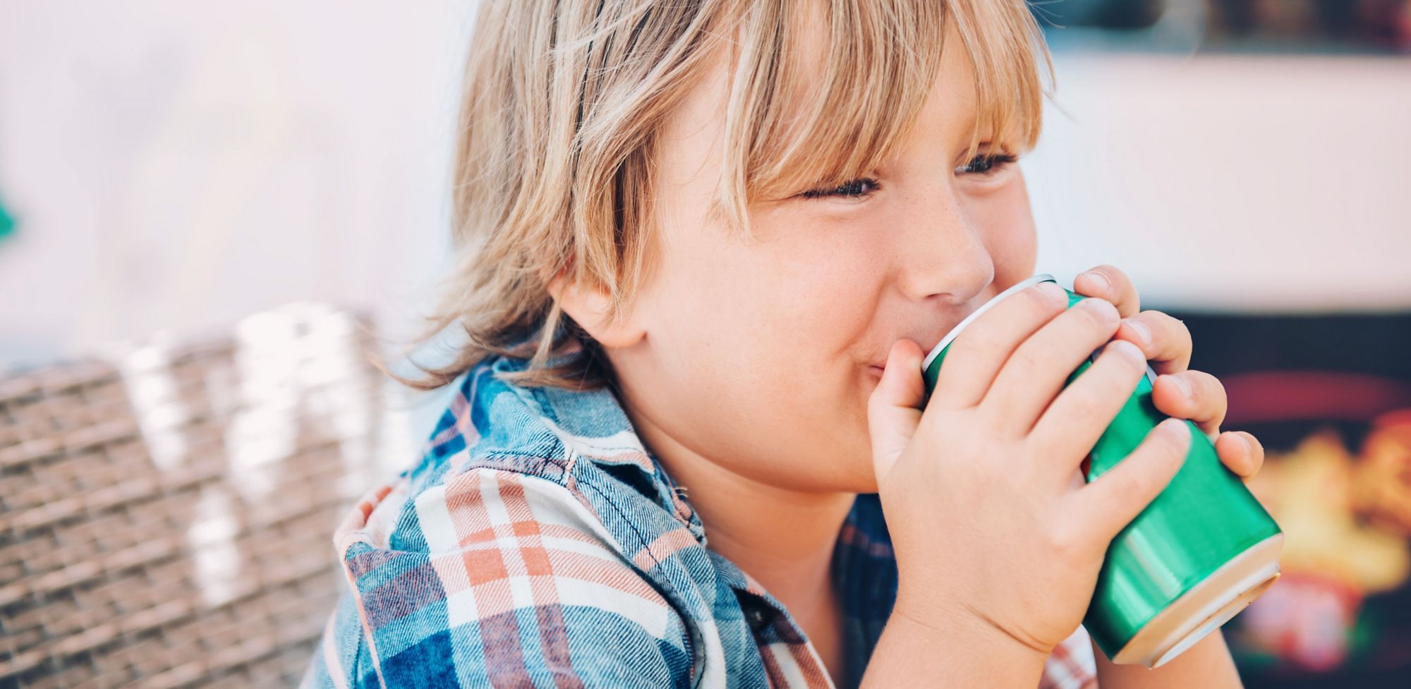 A boy takes a sip from a metal drink can while sitting outside. 
