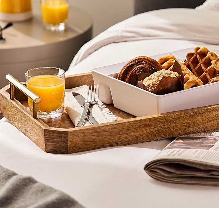 A tray with orange juice and a bento box of baked goods, waffles and fruit.  