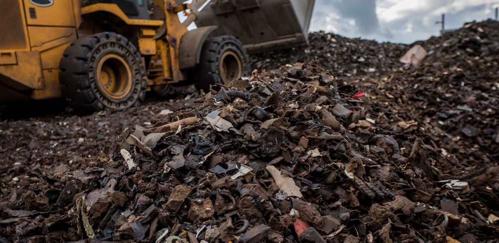 A yellow bulldozer scoops up shreds of automotive waste material to be recycled.  