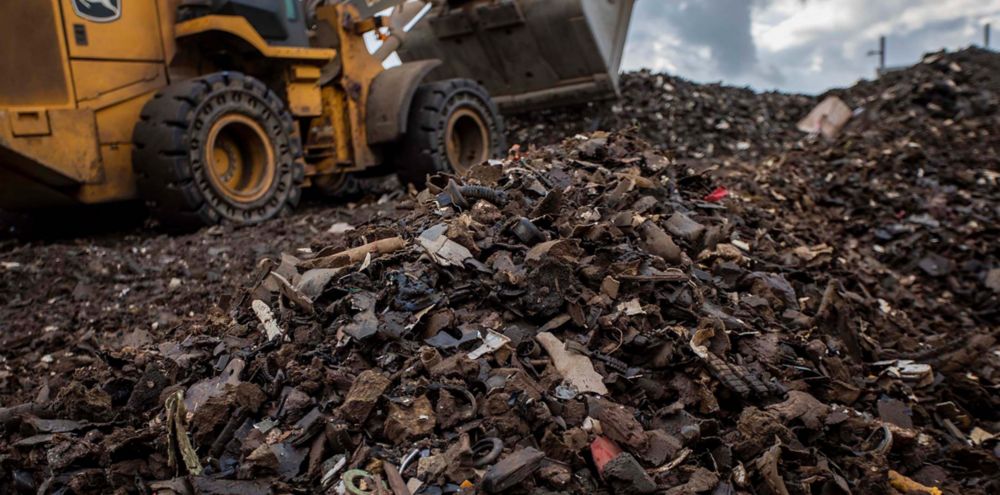 A yellow bulldozer scoops up shreds of automotive waste material to be recycled.  