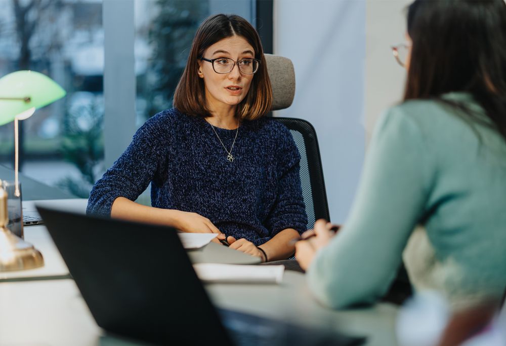 A person in business casual clothing talks to another person.  
