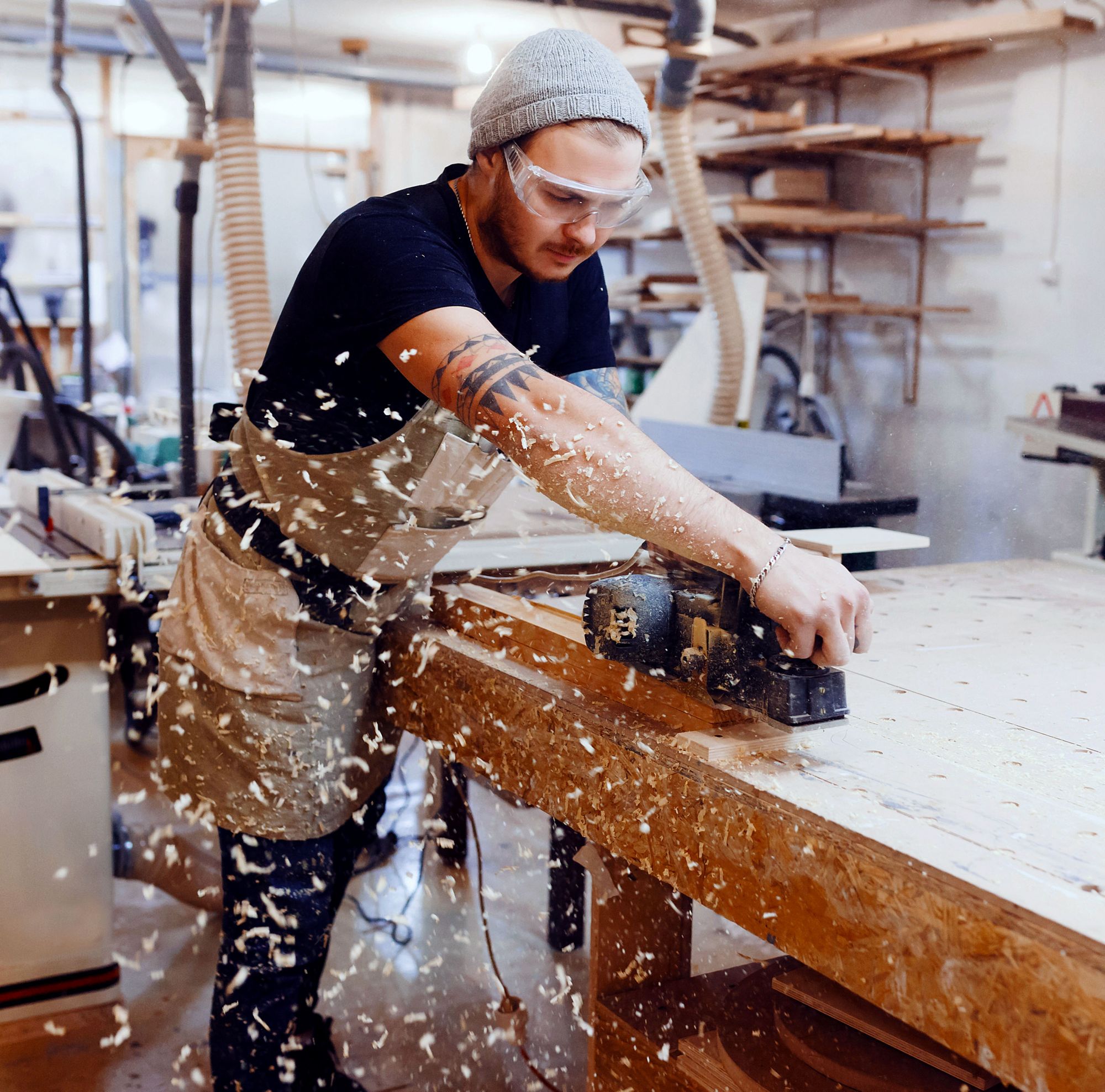 A man in safety glasses saws a block of wood. 
