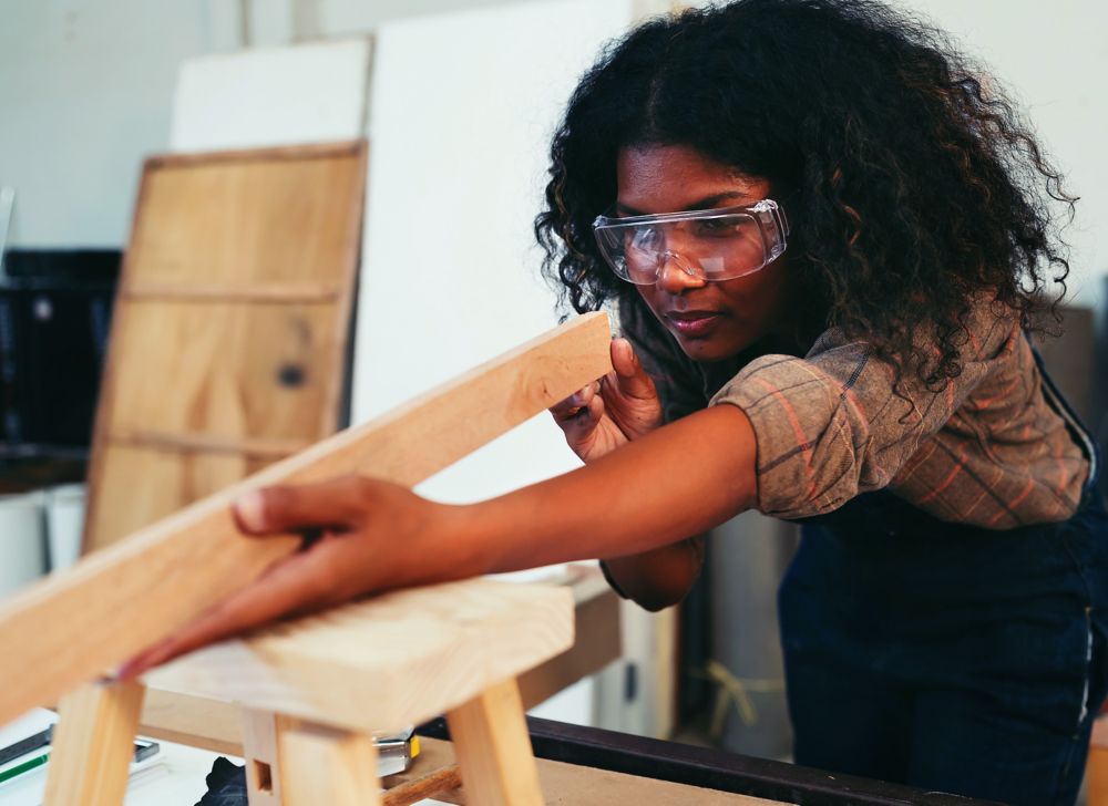 A woman wearing safety goggles as she checks wood quality and level. 