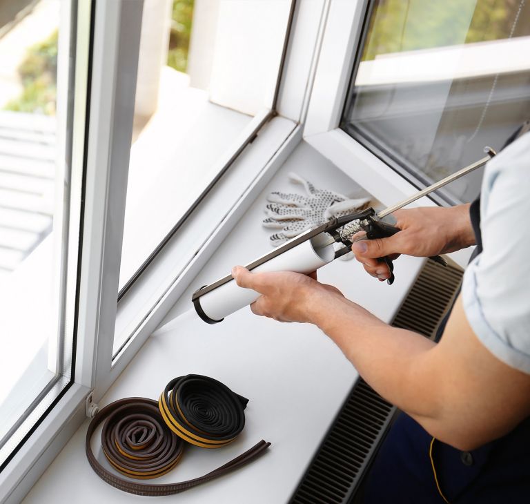 A person caulks a window seal. 