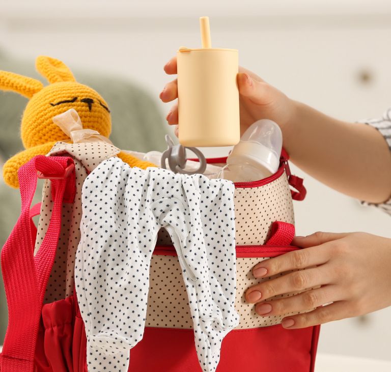 A diaper bag filled with baby clothes, a bottle and toy. 