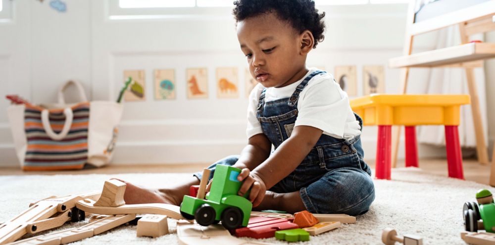 A child plays with a wooden train while sitting on the floor.  