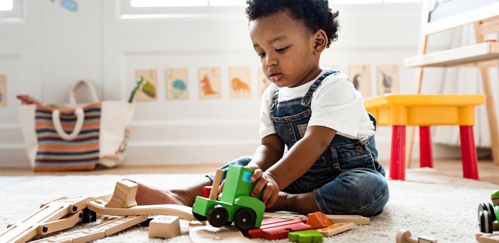 A child plays with a wooden train while sitting on the floor. 