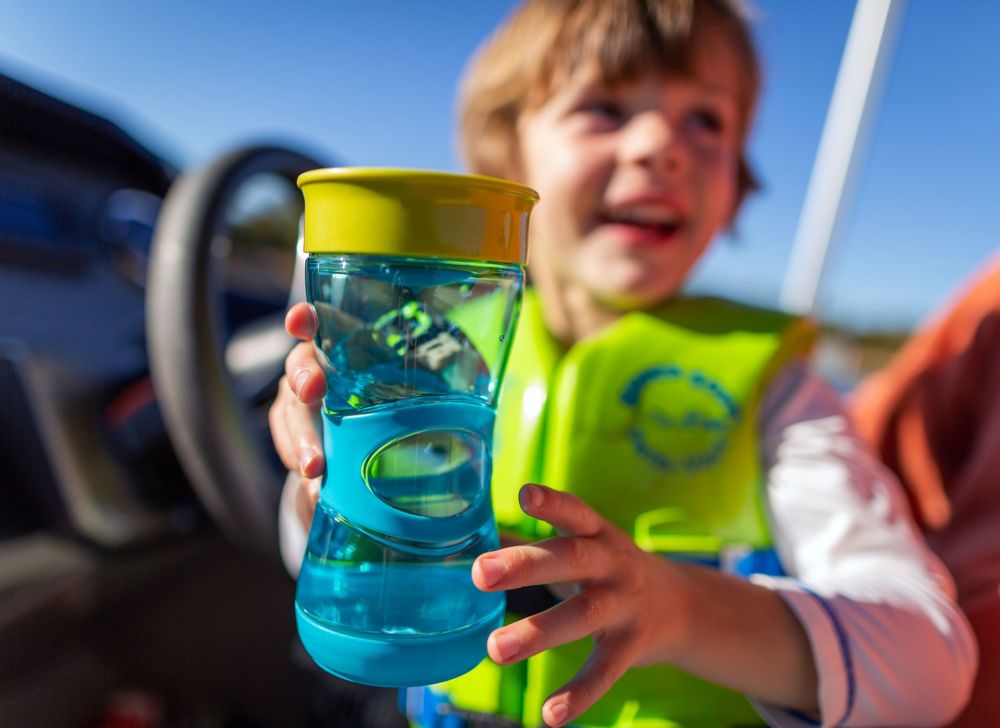 A life vest-wearing child holding a blue and yellow sippy cup. 