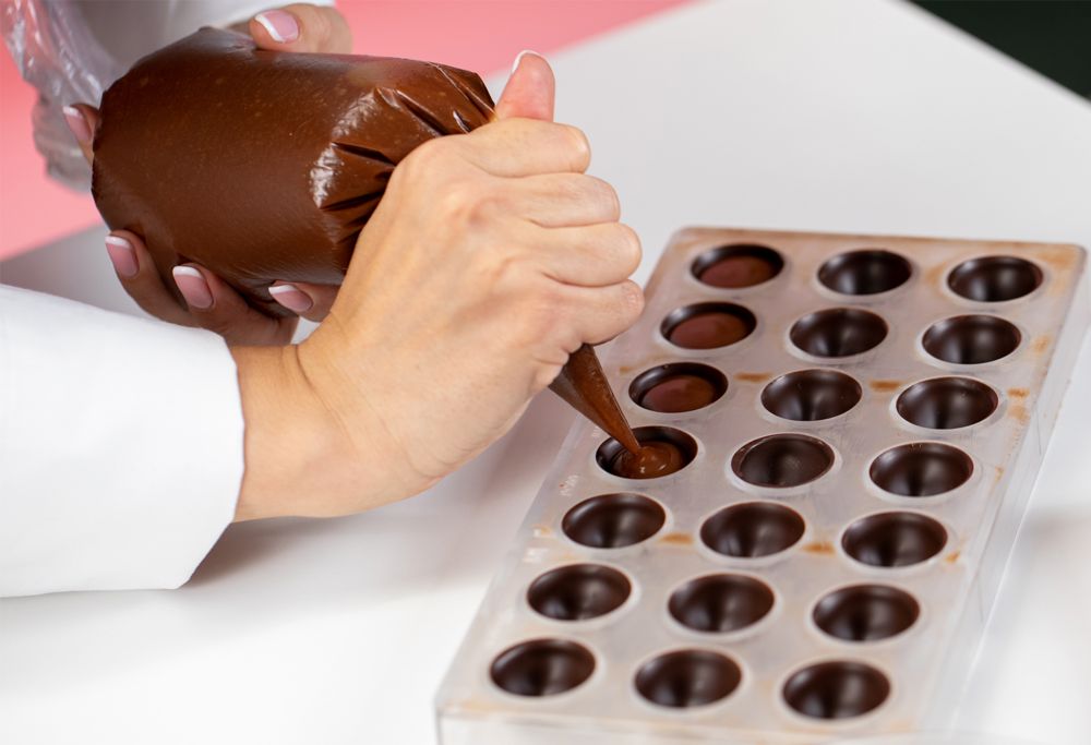 A person uses a bag to pipe molten chocolate into a mold. 