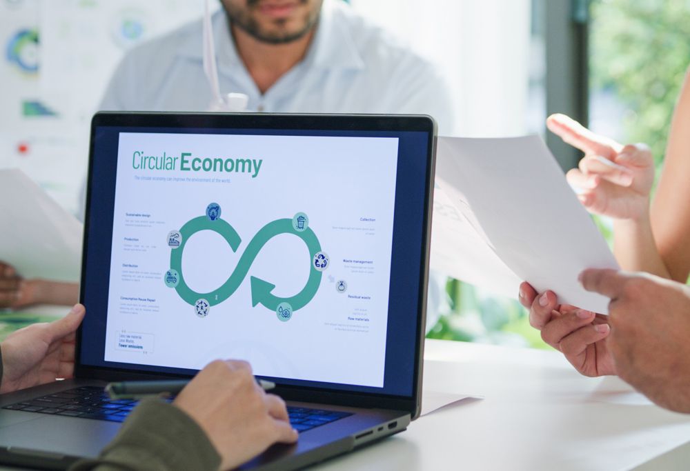 A group of people sits around a laptop, discussing the circular economy while viewing a circular economy diagram.  