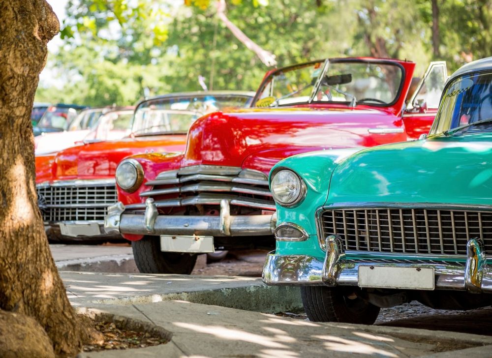 Three antique cars are parked outside for a classic car show. 