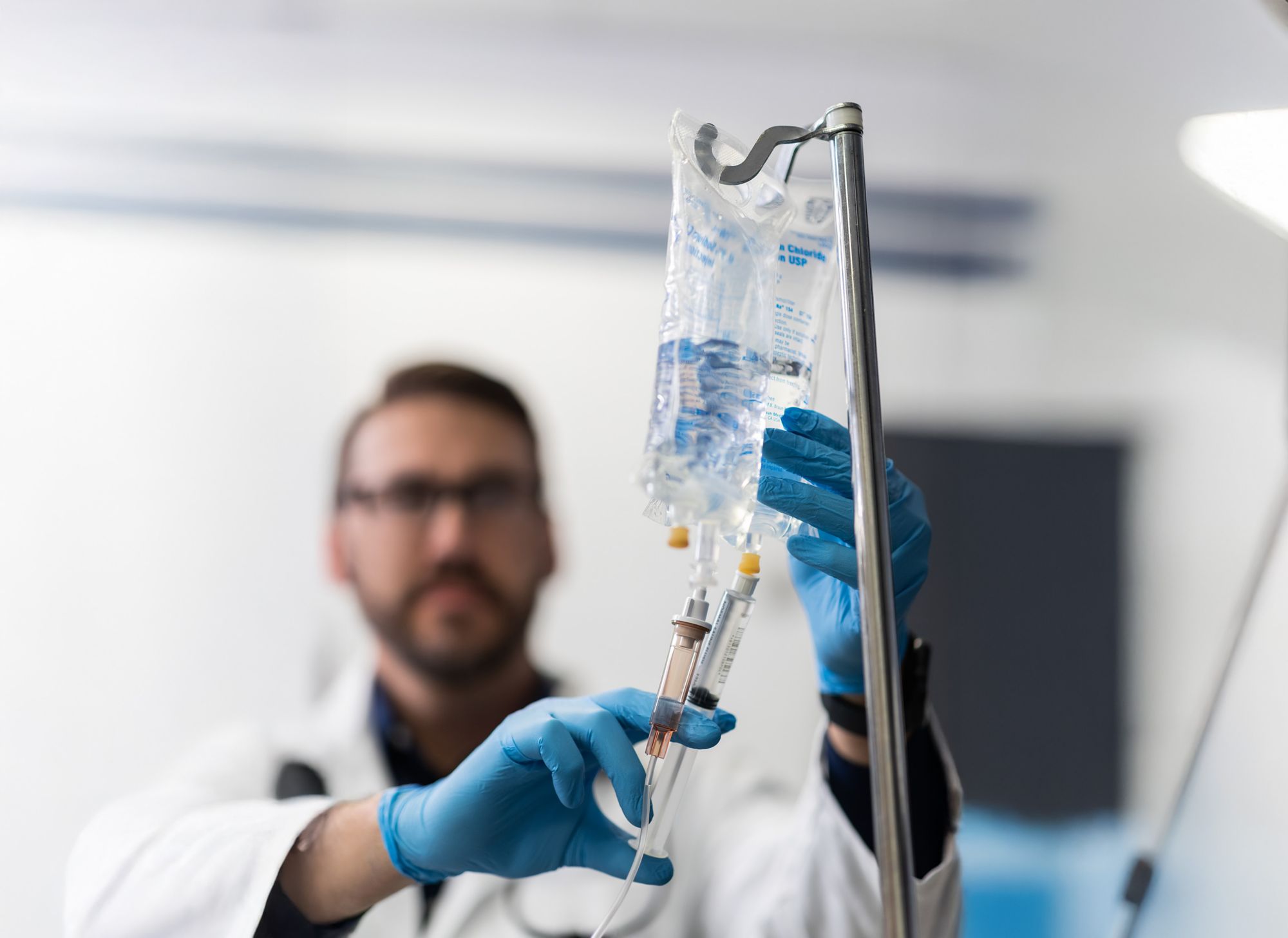 A doctor injects an IV into clear plastic fluids packaging with flexible tubing. 
