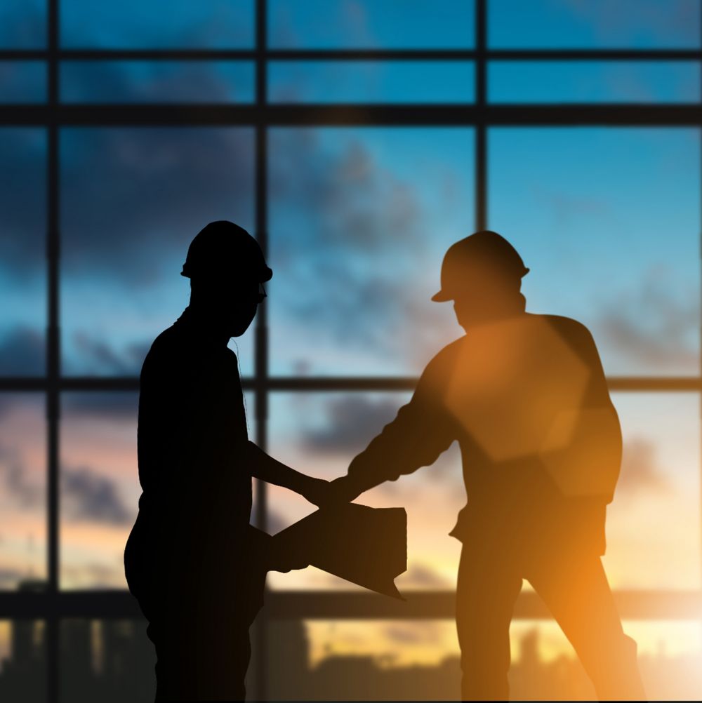 Silhouette of two employees in hard hats examining thermal fluid system plans at a job site.  