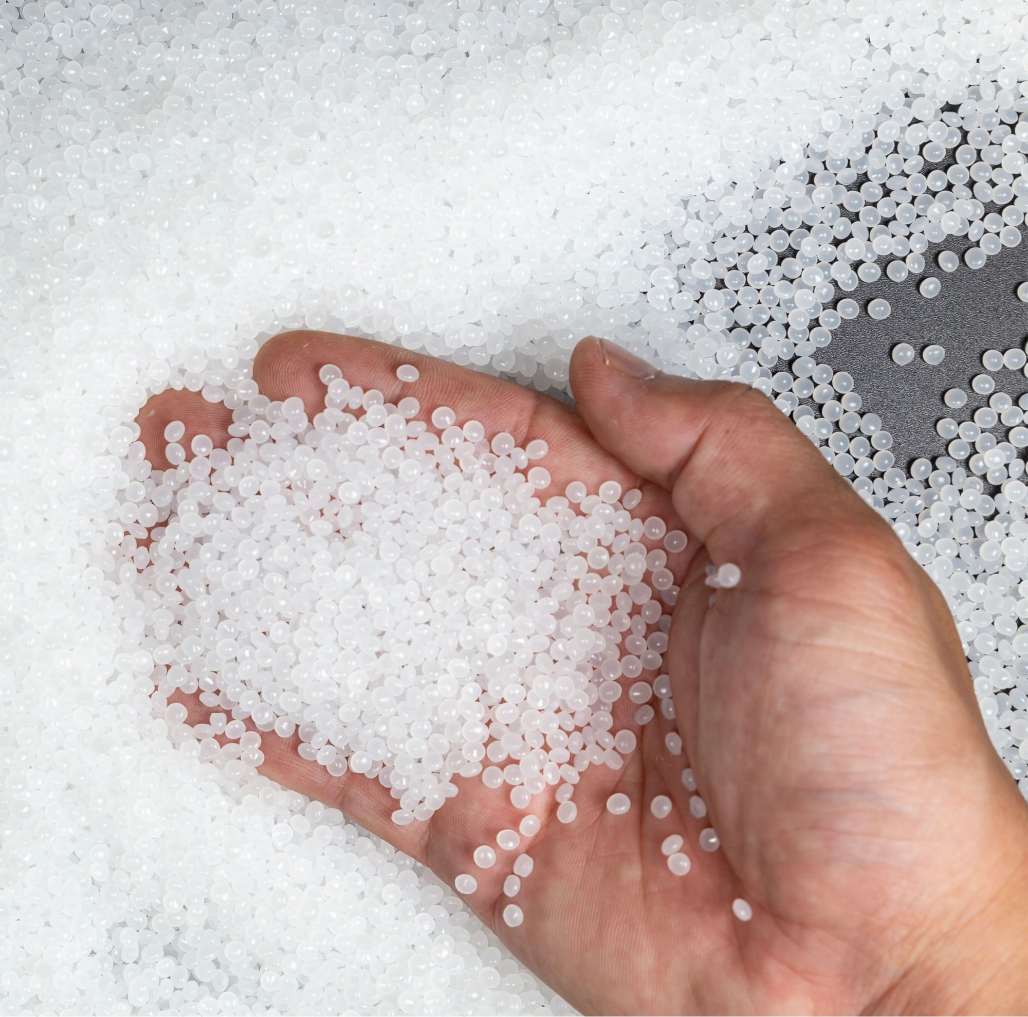 A close-up of a hand holding small white plastic polymer granules. 