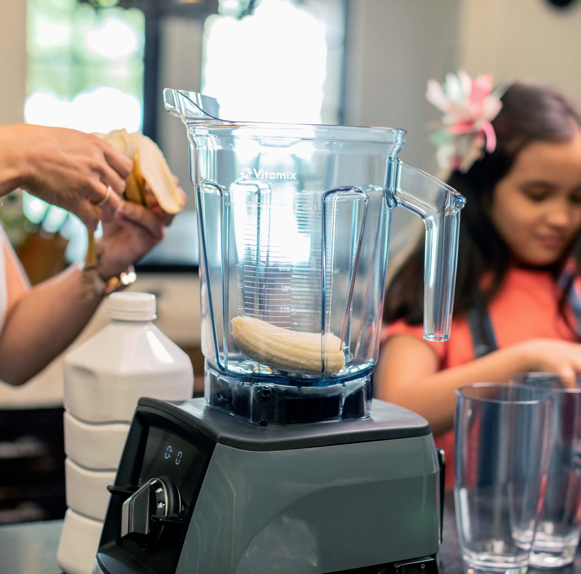 A person putting bananas in a blender that is set on a counter. 