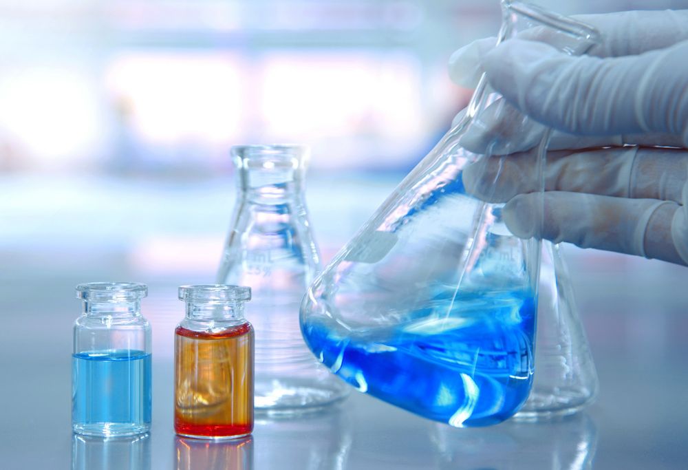 A person holds a beaker of blue liquid 