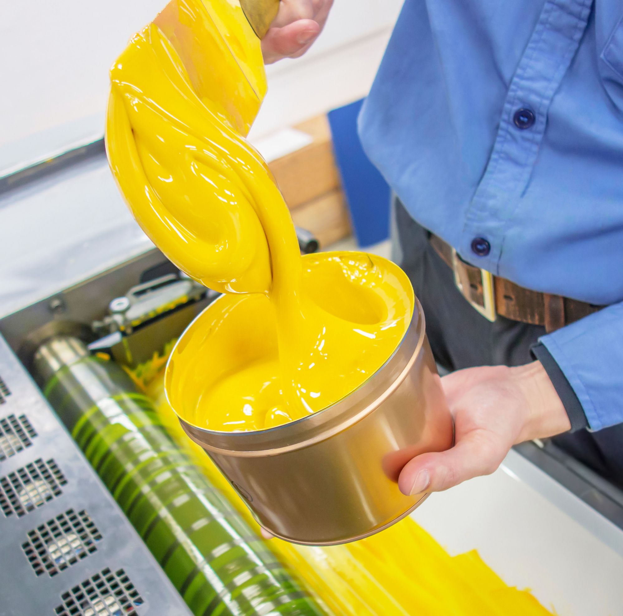 A person applies yellow ink to a press roller. 