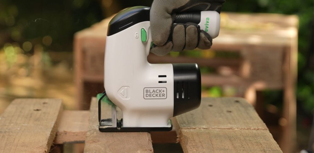 A person wearing gloves, using a Black and Decker Reviva jigsaw to cut a wooden pallet.  